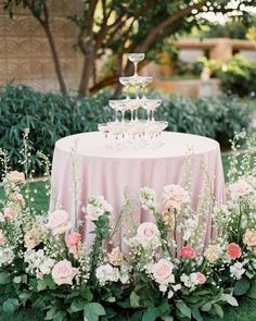 an image of a table with flowers and wine glasses on it in front of some bushes