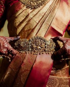 a woman wearing a gold and red sari with intricate jewelry on her hands,