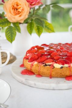 a cake with strawberries on it sitting on a table next to a cup and saucer