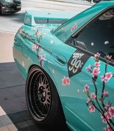 a blue car with pink flowers painted on it's side parked in front of a curb