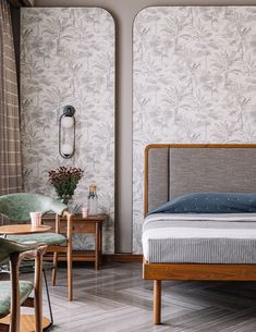 a bed sitting next to a wooden table and chairs in a room with floral wallpaper