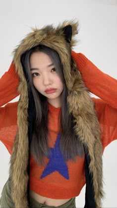 a young woman wearing an orange sweater with a blue star on the front and a furry hood over her head