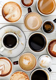 there are many different types of coffees in cups on the white table top with spoons