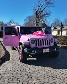 a pink jeep with a bow on the hood parked in front of a driveway area