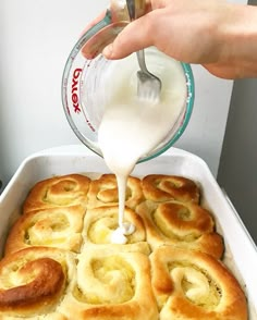 someone pouring milk into a pan filled with rolls