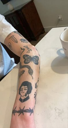 a person with tattoos on their arm sitting at a table next to a coffee cup