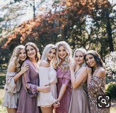 a group of women standing next to each other posing for a photo in front of trees