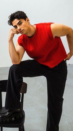 a man sitting on top of a black chair next to a white wall and holding his hand near his face