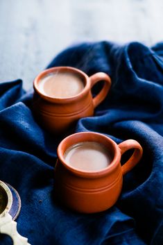 two orange mugs filled with liquid on top of a blue cloth