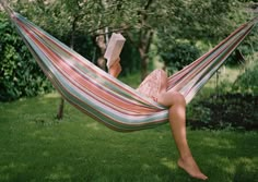 a woman laying in a hammock reading a book