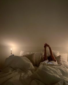 a woman laying in bed with her arms up above her head and two candles on either side