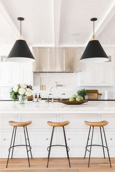 three stools sit at the center of a large kitchen island with marble countertops and white cabinets