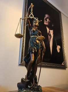 a statue of lady justice holding the scales of justice in front of a framed portrait