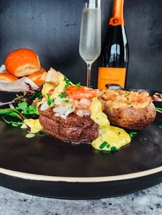 a black plate topped with meat and veggies next to a bottle of wine