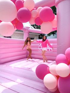 two women are dancing in an inflatable pool with pink and white balloons hanging from the ceiling