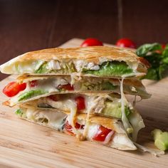 a cut in half sandwich sitting on top of a cutting board next to tomatoes and lettuce