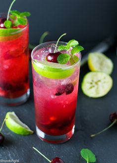 two glasses filled with red and green drinks on top of a black table next to sliced fruit