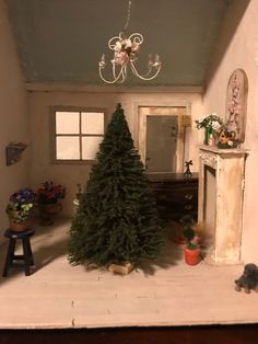 a miniature christmas tree in the corner of a room with a chandelier hanging from the ceiling