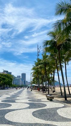 an empty street lined with palm trees next to the ocean and tall buildings in the background