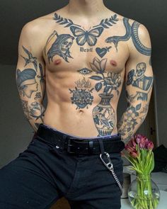 a man with tattoos on his chest standing next to a vase filled with pink flowers