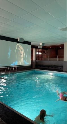 two people in a swimming pool watching a movie on the wall behind them is a projector screen