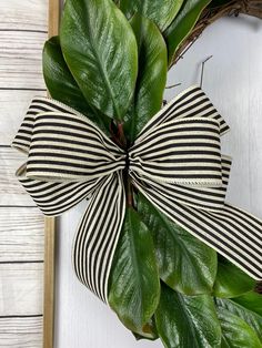 a green wreath with black and white striped bow hanging on the front door, next to a wooden frame