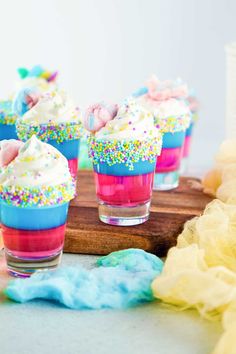 small cupcakes with sprinkles and colored frosting are on a wooden board