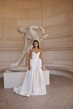 a woman standing in front of a statue wearing a white dress and holding a baseball bat