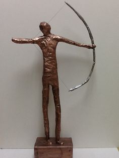 a statue of a man holding a bow and arrow in his hand, on top of a wooden block