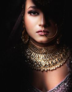 a woman wearing a gold necklace and choker with her nose ring in the dark