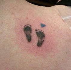 a woman's lower back tattoo with two footprints and a blue heart