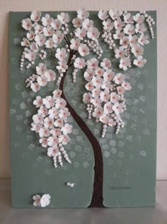 a tree with white flowers on it sitting on top of a table next to a wall