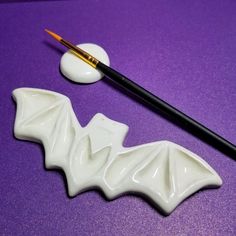 a white bat shaped object next to a paintbrush on a purple surface with a yellow tip