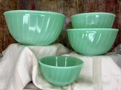 three green glass bowls sitting on top of a white cloth next to a wooden wall