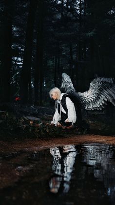 a woman with white hair and an angel wings is sitting on the ground next to a body of water