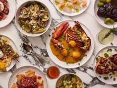 a table topped with lots of plates and bowls filled with different types of food next to utensils