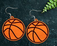 pair of basketball earrings on black background with green plant in the corner, top view