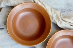 two brown plates sitting next to each other on a marble counter top with napkins