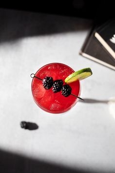 a red drink with blackberries and cucumber garnish