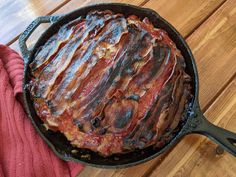 a cast iron skillet filled with bacon on top of a wooden table next to a red towel