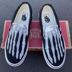 a pair of black and white shoes with skeleton hand painted on the soles, sitting in front of a box