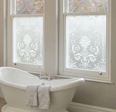 a white bath tub sitting next to two windows in a bathroom with an ornate design on the window sill