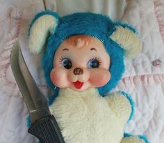 a teddy bear laying on top of a bed next to a large knife in it's mouth