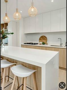 a kitchen with white counters and stools next to a counter top that has three lights hanging above it