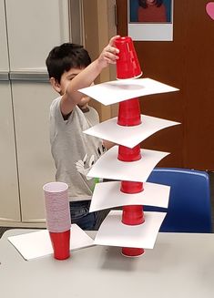 a young boy is playing with a tower made out of plastic cups and paper plates