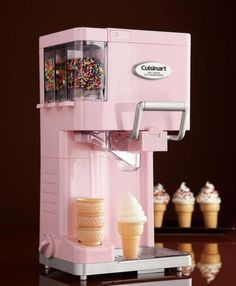 a pink ice cream machine sitting on top of a counter next to cupcakes