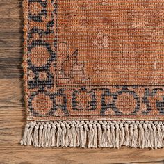 an orange and blue rug with fringes on top of a wooden floor next to a wall