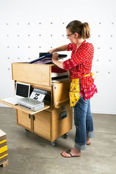 a woman standing next to a desk with a laptop on it and an open drawer in front of her