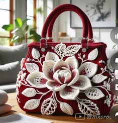 a red handbag sitting on top of a wooden table next to a white flower