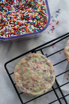 sprinkle covered cookies on a cooling rack next to a container of sprinkles